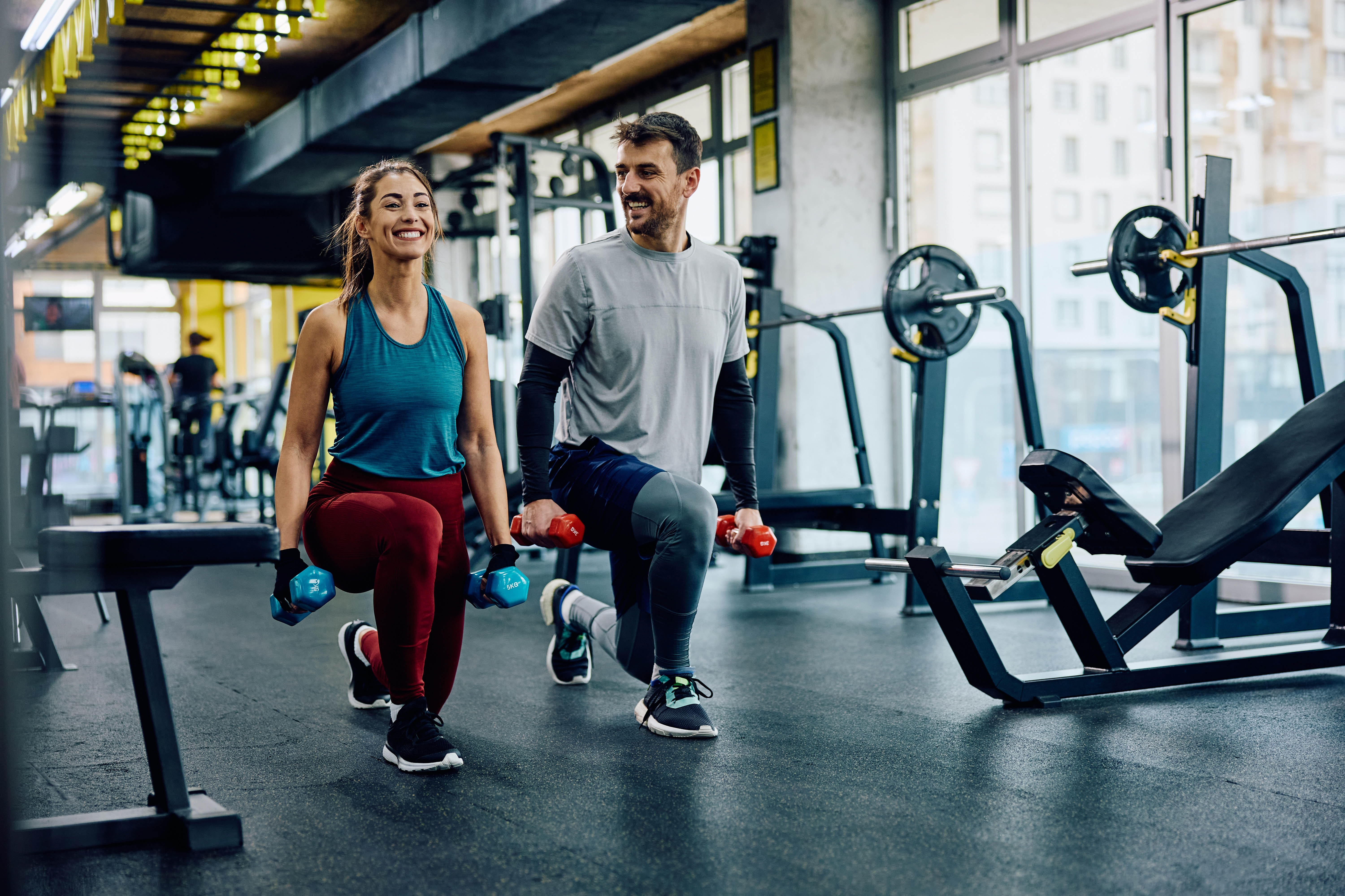 Young couple working out together in the gym, smiling at each other as they complete a set of lunges Young couple working out together in the gym, smiling at each other as they complete a set of lunges
